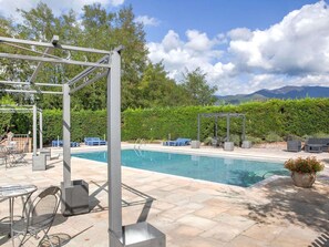 A pool area with a pergola, lounge chairs, and a view of mountains.