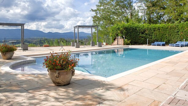 Ett poolområde med fri utsikt över bergen i bakgrunden, en pergola och krukväxter.