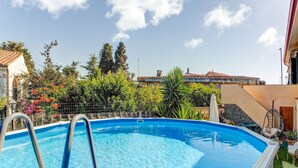 Una piscina con escalera metálica, rodeada de abundante follaje y un cielo despejado.