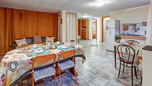 Un comedor con una mesa dispuesta para cuatro, una cocina equipada con refrigerador y una sala de estar con sofá y cortinas.
