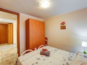 Quarto com uma cama, um guarda-roupa de madeira, um quadro na parede e um banheiro visível através de uma porta aberta.