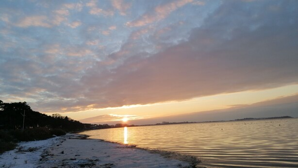 Tramonto su un mare calmo con una costa in lontananza.