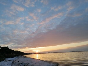 Um pôr do sol sobre águas calmas, com uma linha de costa distante.