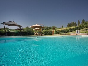 A clear blue pool with lounge chairs and umbrellas, surrounded by greenery and a hilly landscape. - Cottage in Tuscany With Pool and Sauna (Terranuova Bracciolini)