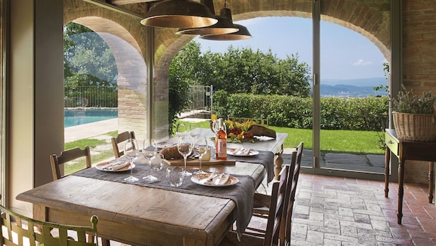 A dining area with a table set for four, overlooking a landscaped garden and pool. - Villa in Arezzo With Pool and Vineyards (Arezzo)
