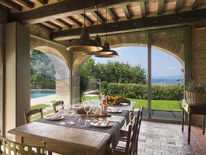 Un espace repas avec une table dressée pour quatre personnes, donnant sur un jardin aménagé et une piscine.