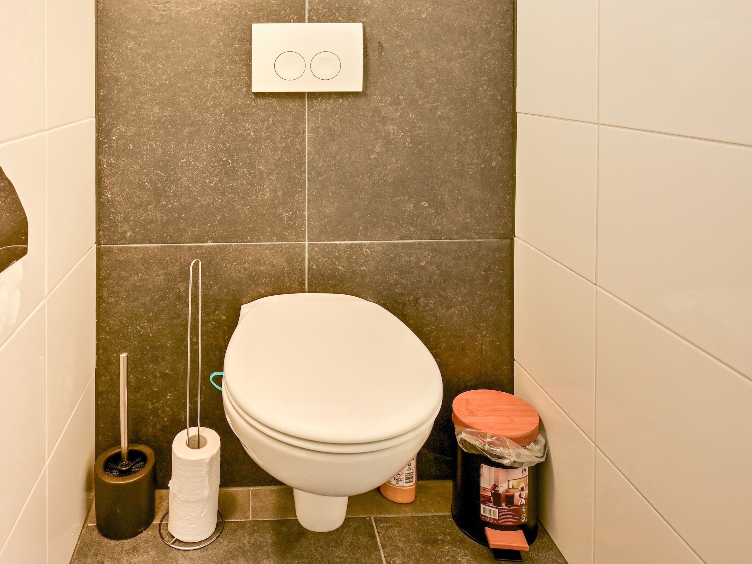 Ein Badezimmer mit Toilette, WC-Bürste, Toilettenpapier und Mülleimer.