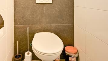 Ein Badezimmer mit Toilette, WC-Bürste, Toilettenpapier und Mülleimer.