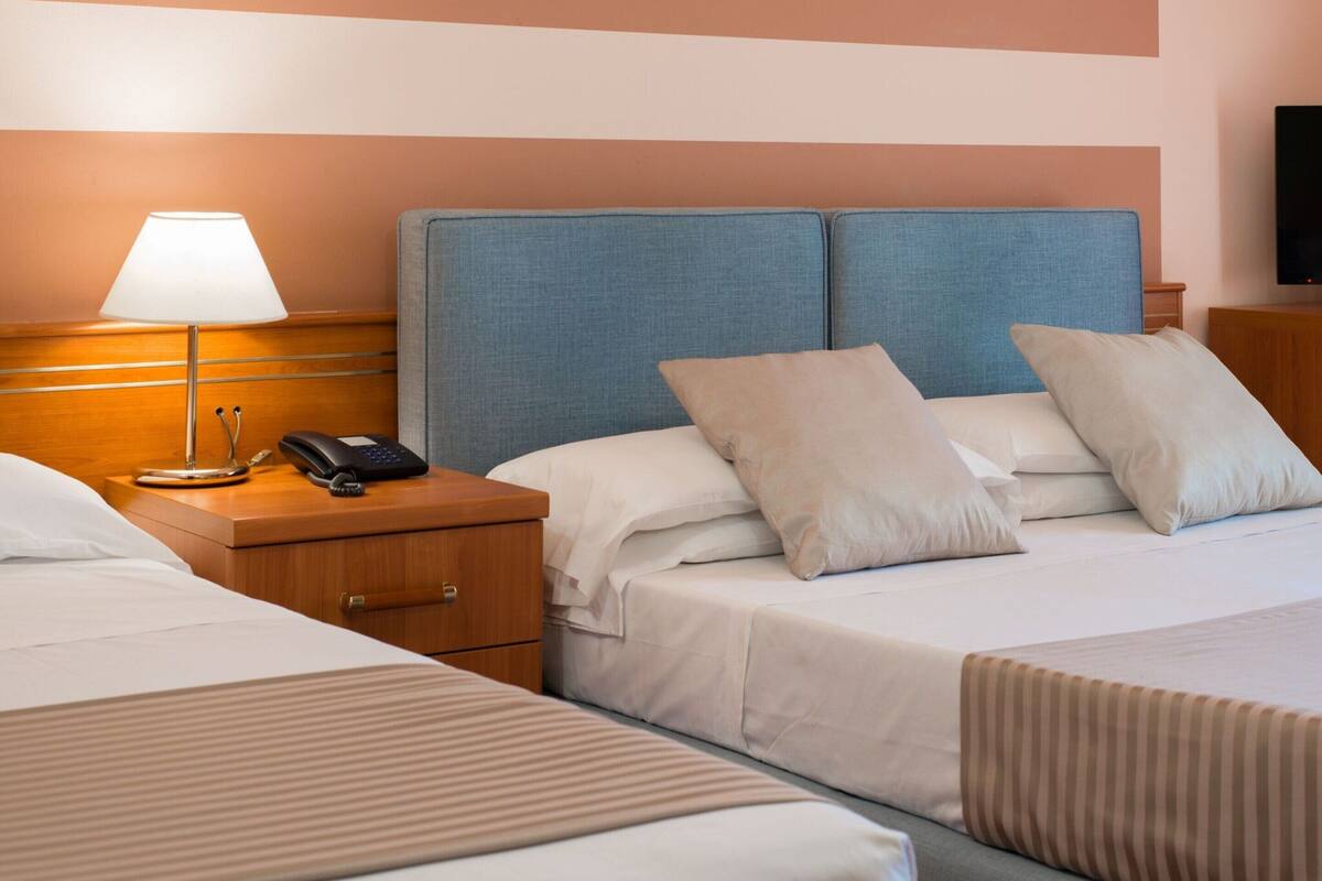 Ein Hotelzimmer mit zwei Betten, einem Nachttisch mit Lampe, einem Telefon und einem Fernseher auf einem Schrank.