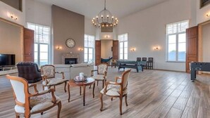 A spacious living room with a fireplace, a pool table, and a large chandelier.