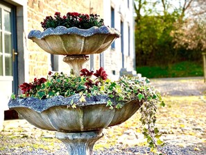 Stunning stone fountain features a tiered design with lush plants and flowers.