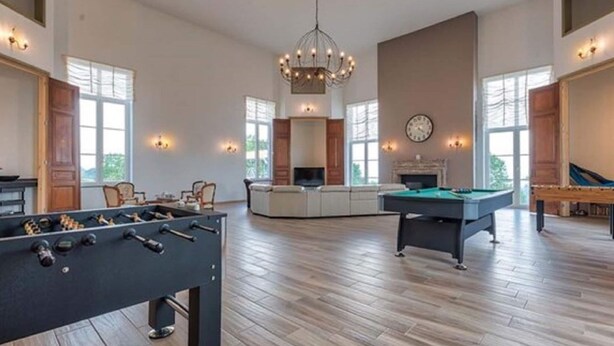 A spacious living room with a foosball table, pool table, and a large chandelier.