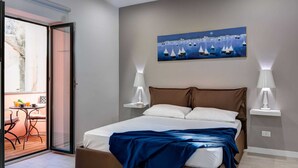 Un dormitorio con cama, lámparas de noche, un cuadro y un balcón con mesa y sillas.