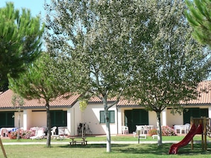 A building with a tiled roof, outdoor seating, and a playground. - Semi Detached Bungalow with AC near Coast of Tuscany (Campiglia Marittima)