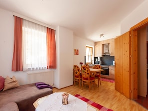 Un salon avec un canapé, une table à manger avec des chaises, un coin cuisine avec une cuisinière et un évier, et une armoire en bois.