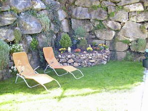 Two lounge chairs positioned in front of a stone wall with a flower bed. - Apartment in Gerlosberg Near Ski Lift (Gerlosberg)