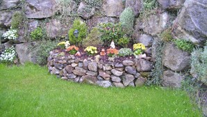 A garden with a stone wall, various plants, and a gnome statue. - Apartment in Gerlosberg Near Ski Lift (Gerlosberg)