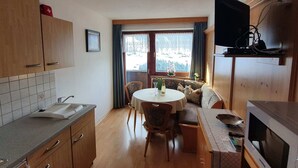 A compact kitchen with wooden cabinets, a built-in microwave, and a dining area with a round table and chairs. - Apartment in Gerlosberg Near Ski Lift (Gerlosberg)