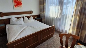 A hotel room with a large bed, wooden headboard, white bedding, a bedside table, a chair, and a window with sheer curtains. - Apartment in Gerlosberg Near Ski Lift (Gerlosberg)