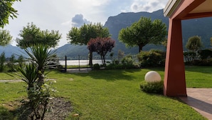 A well-maintained garden with a variety of trees, a large spherical sculpture, and a view of mountains in the background. - Villa by Lake Idro With Panoramic Views (Idro)
