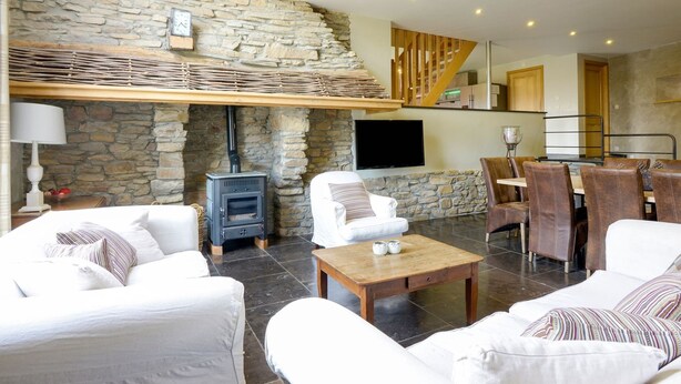 A modern living room with stone walls, a fireplace, a TV, and a dining area with wooden furniture. - Magnificent Holiday Home in Manhay With Fenced Garden (Manhay)