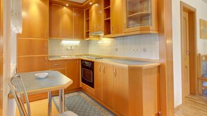 A compact kitchen with wooden cabinets, a built-in oven, and a dining area with a table and chairs. - Lovely Apartment in Bled near Lake (Bled)