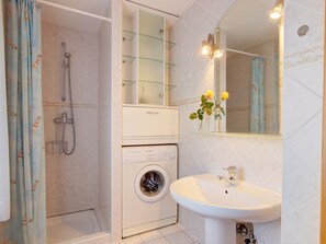 A bathroom with a shower, a washing machine, a sink, and a mirror.