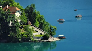 A lakeside property with a dock, a white building with a red roof, and boats on the water. - Lovely Apartment in Bled near Lake (Bled)