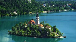 Une petite île avec une église et quelques bâtiments, entourée d’un lac et de collines boisées.