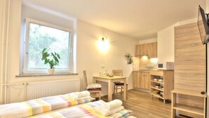 Une pièce de taille modeste comprenant un lit, une petite kitchenette, un coin repas et une fenêtre avec des stores.