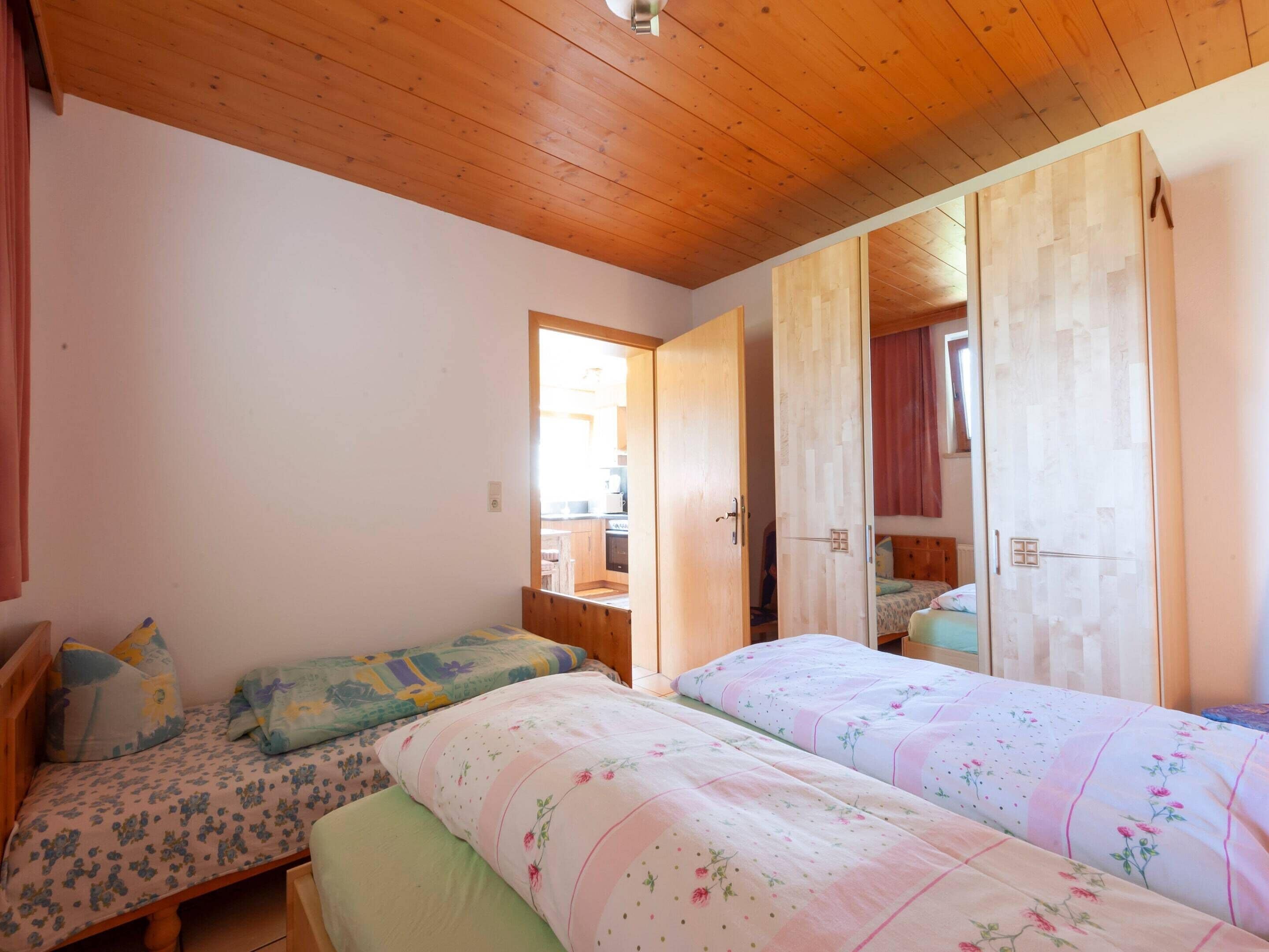 A bedroom with two beds, wooden ceiling, and a door leading to a kitchen.