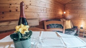 A wooden cabin interior with a dining table set for two, a bottle of champagne, and a vase with yellow flowers. - Cozy Holiday Apartment Close to the Slopes (Kleinarl)