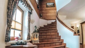 A wooden staircase with a lantern on the landing, a window with curtains, and a small shelf with decorative items. - Cozy Holiday Apartment Close to the Slopes (Kleinarl)
