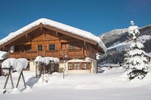 A wooden chalet with a snow-covered roof, surrounded by a snowy landscape and mountains. - Cozy Holiday Apartment Close to the Slopes (Kleinarl)