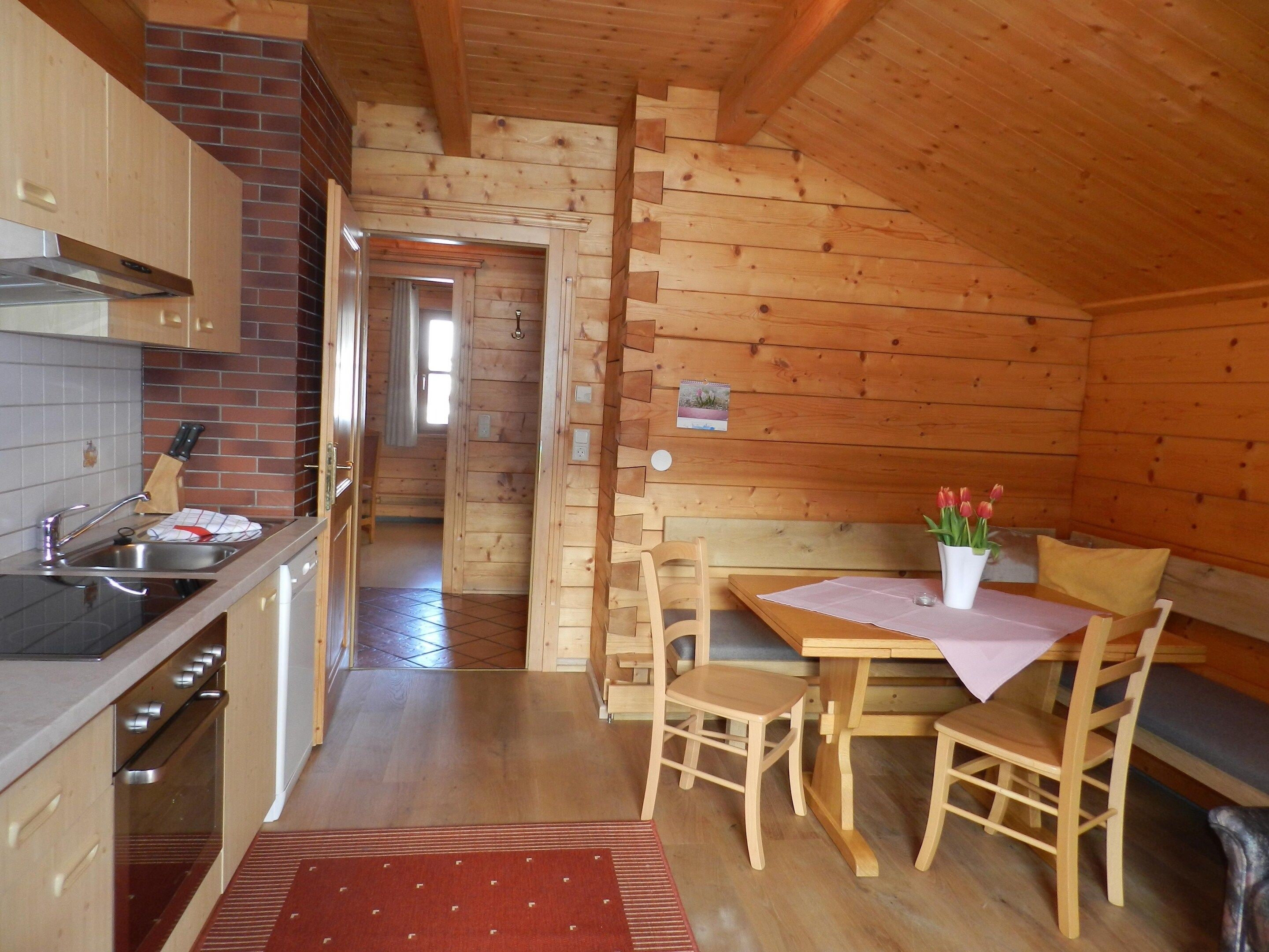 A wooden cabin interior with a kitchen, dining area, and a visible bathroom.
