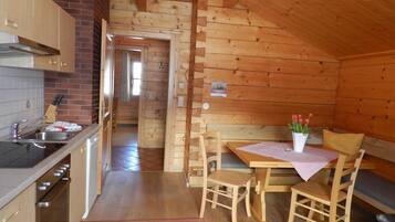 A wooden cabin interior with a kitchen, dining area, and a visible bathroom.