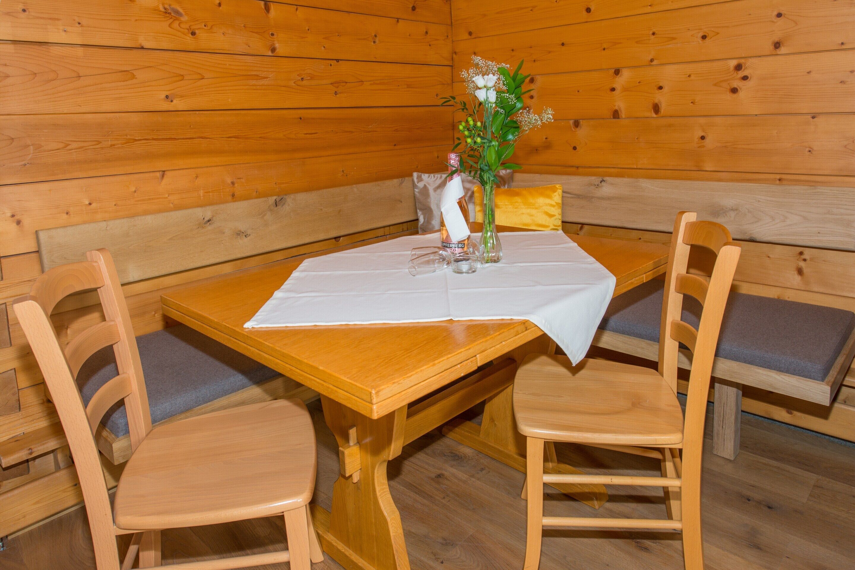 A wooden cabin interior with a dining table set for two, surrounded by wooden chairs with cushioned seats.