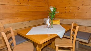 Een houten hutje interieur met een eettafel voor twee personen, omringd door houten stoelen met beklede zitplaatsen.