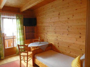 A wooden cabin room with a single bed, a table with a bottle, and a chair. - Cozy Holiday Apartment Close to the Slopes (Kleinarl)