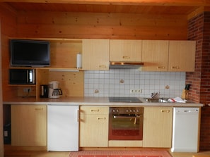 Una cocina compacta con armarios de madera, microondas, cafetera, estufa y lavavajillas.