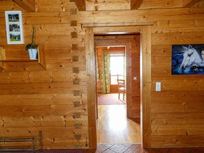 A wooden interior with a doorway leading to another room, a wall-mounted shelf with a plant, and a painting of horses. - Cozy Holiday Apartment Close to the Slopes (Kleinarl)