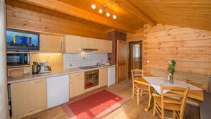 Een houten blokhut interieur met een keuken, een eethoek en een televisie waarop een sportevenement wordt vertoond.