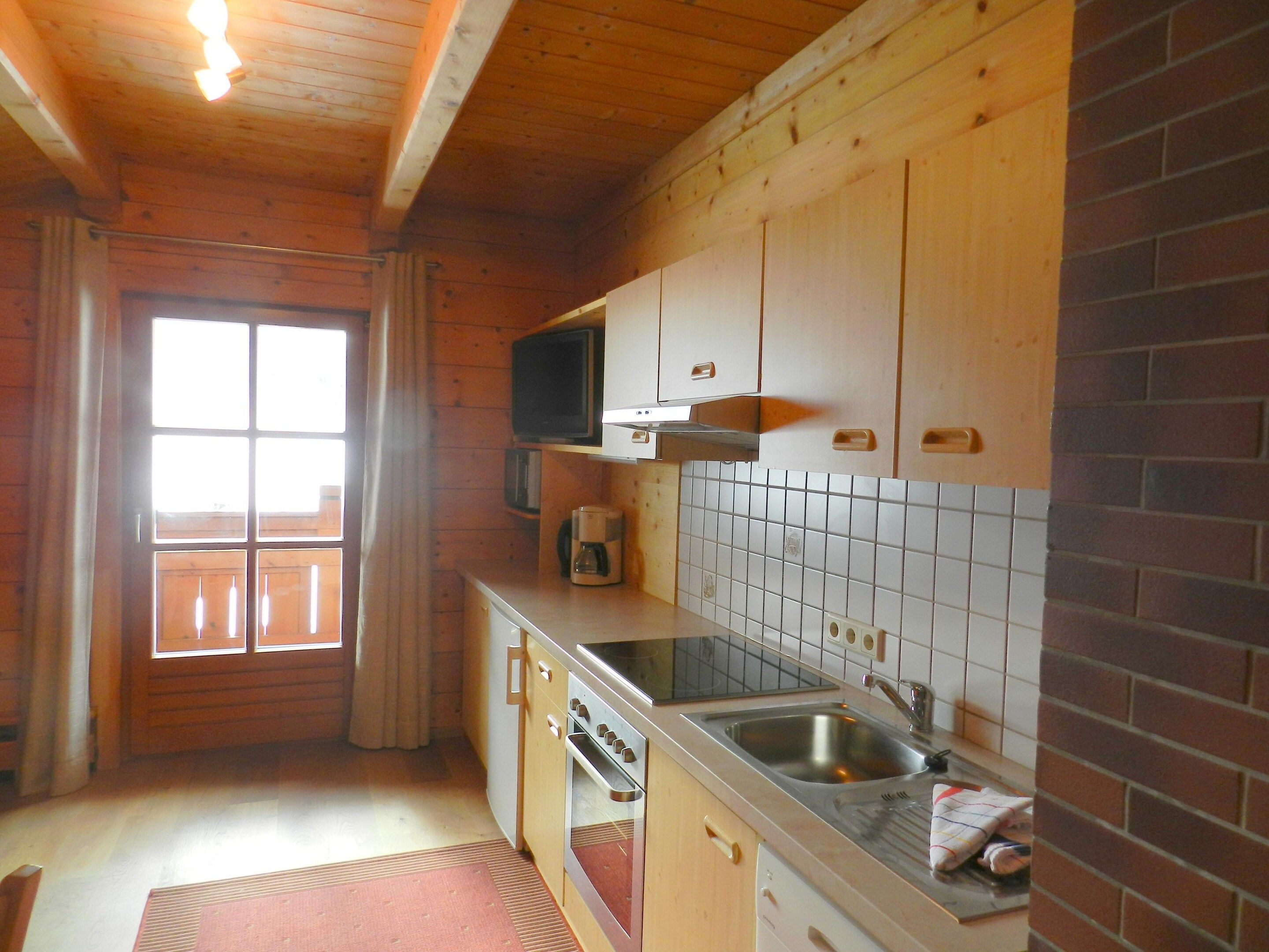 Eine kompakte Küche mit Holzschränken, einer eingebauten Mikrowelle, einem Edelstahl-Spülbecken und einer gefliesten Rückwand.