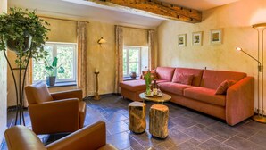A cozy living room with a red sofa, leather armchairs, a coffee table, and a large window with curtains. - Spacious Apartment in a 16th-century Castle (Aywaille)