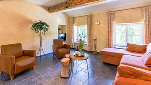A spacious living room with a fireplace, leather sofas, a coffee table, and a large window providing natural light. - Spacious Apartment in a 16th-century Castle (Aywaille)