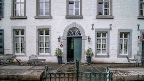 A white building with a green door, multiple windows, and outdoor seating. - Spacious Apartment in a 16th-century Castle (Aywaille)