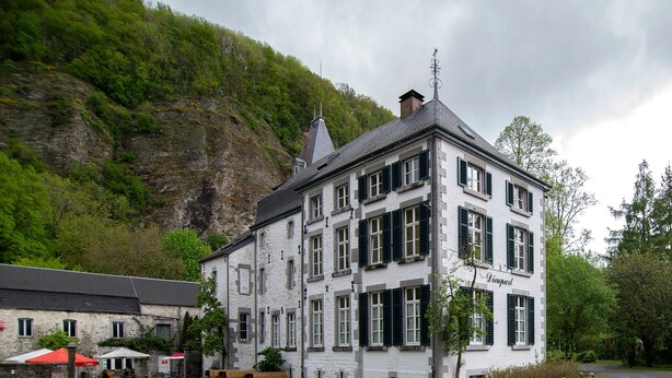 A white building with multiple windows and a chimney, surrounded by greenery and a gravel area with benches. - Spacious Apartment in a 16th-century Castle (Aywaille)