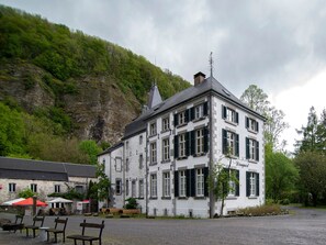 Un bâtiment blanc doté de nombreuses fenêtres et d’une cheminée, entouré de verdure et d’un espace recouvert de gravier, agrémenté de bancs.