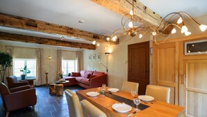 A dining area with a long wooden table set for two, flanked by chairs, in a room with exposed wooden beams and a cozy atmosphere. - Spacious Apartment in a 16th-century Castle (Aywaille)