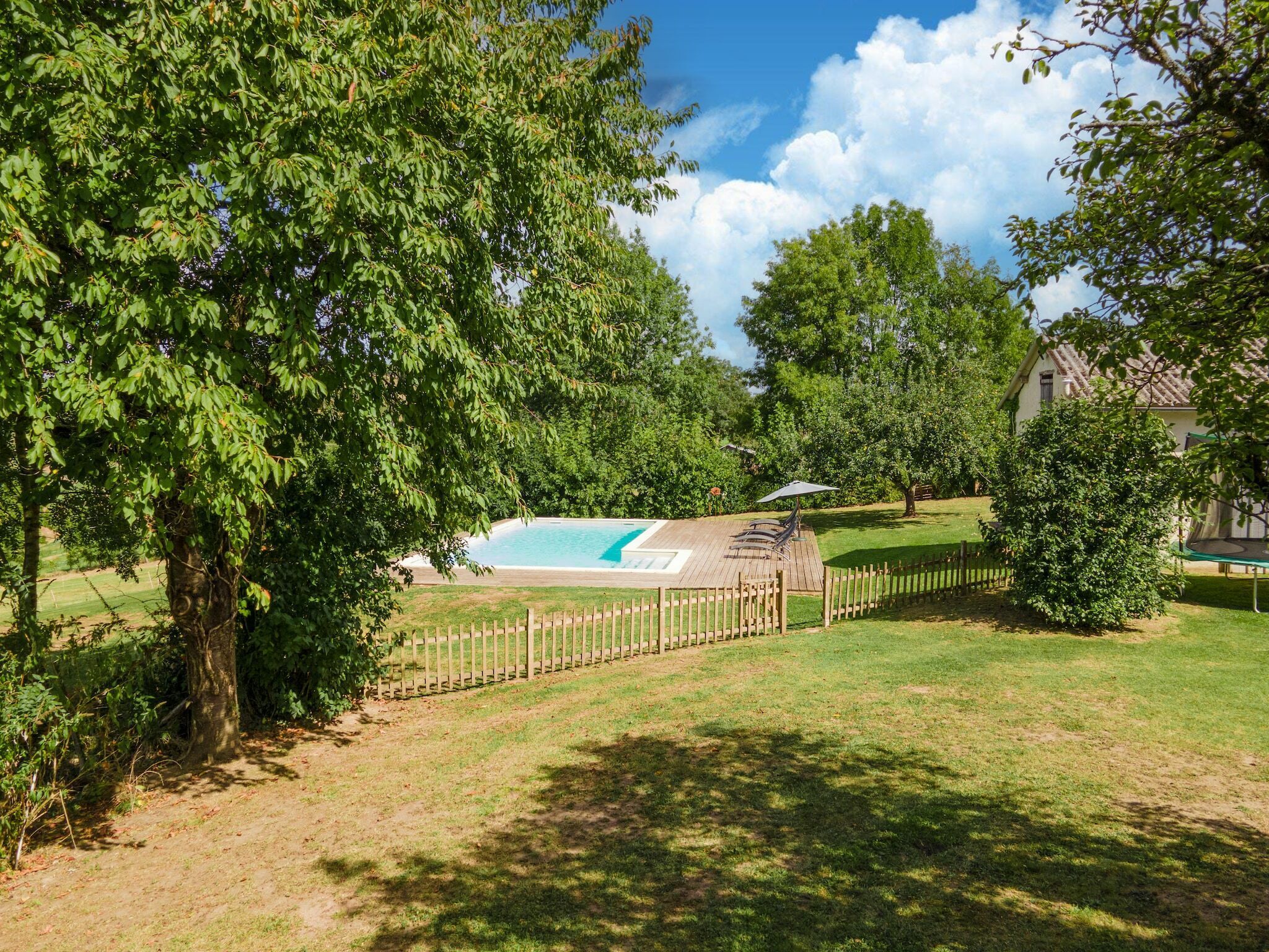 Ein Garten mit Schwimmbad, Holzterrasse und umzäunter Fläche.